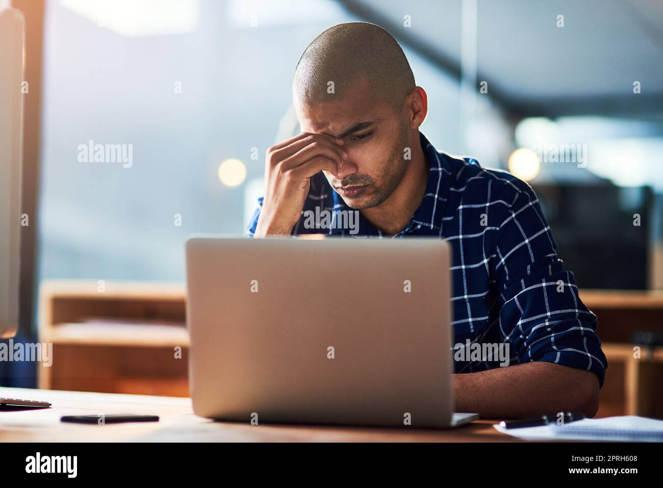 HES hat Schwierigkeiten, mit den Anforderungen der Arbeit Schritt zu halten. Ein junger Designer sieht gestresst aus, während er an seinem Schreibtisch arbeitet. Stockfoto