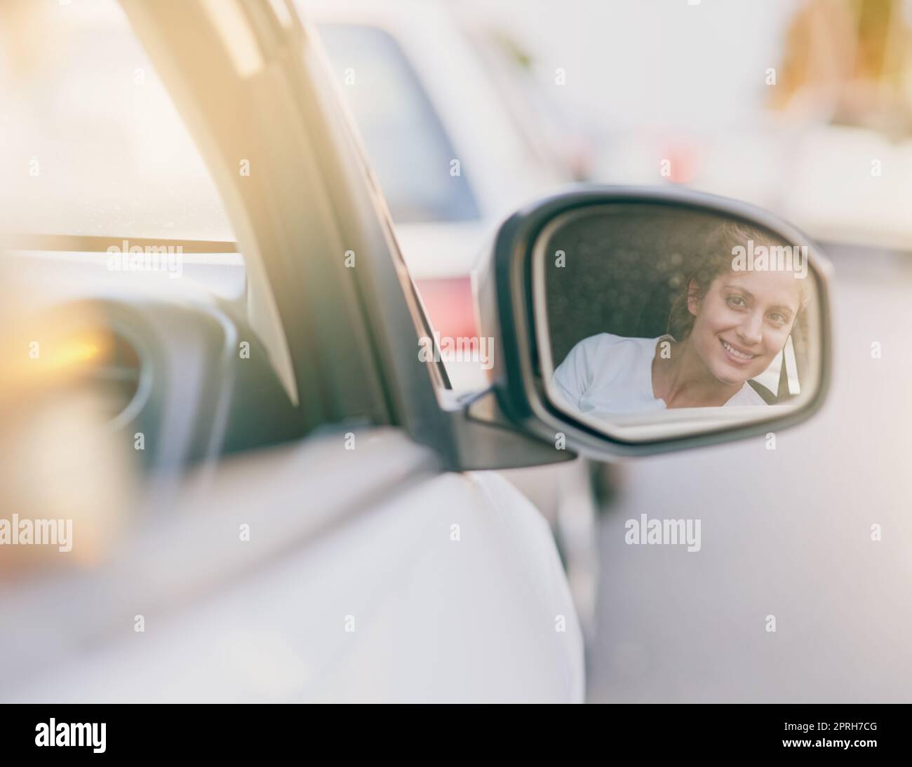 Wachsamkeit sorgt für Sicherheit auf der Straße. Eine junge Frau schaut während der Fahrt in den Seitenspiegel ihres Autos. Stockfoto