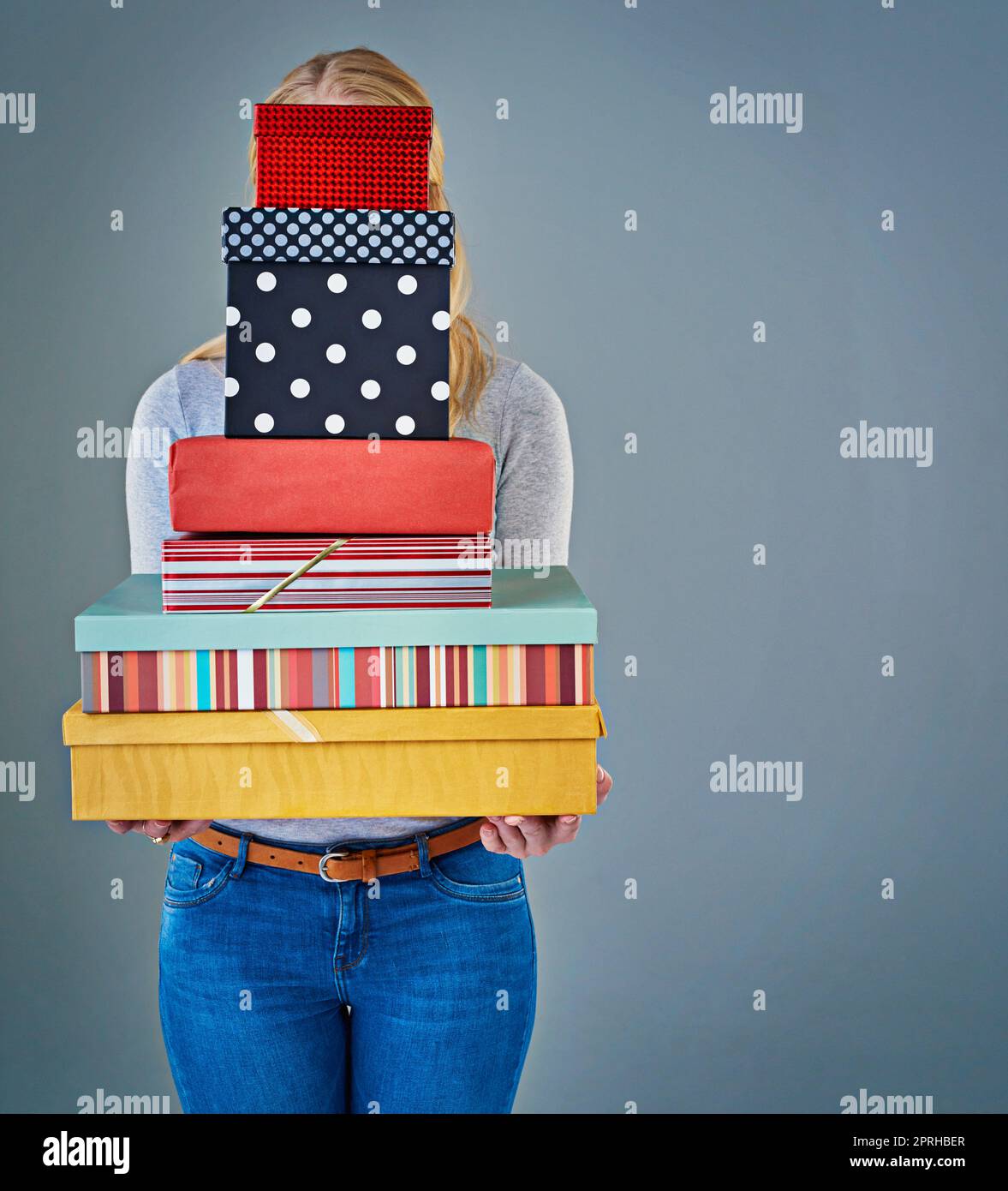 Hinter diesem Stapel von Geschenken. Beschnittene Studioaufnahme einer jungen Frau, die einen Stapel Geschenke vor ihrem Gesicht hält. Stockfoto