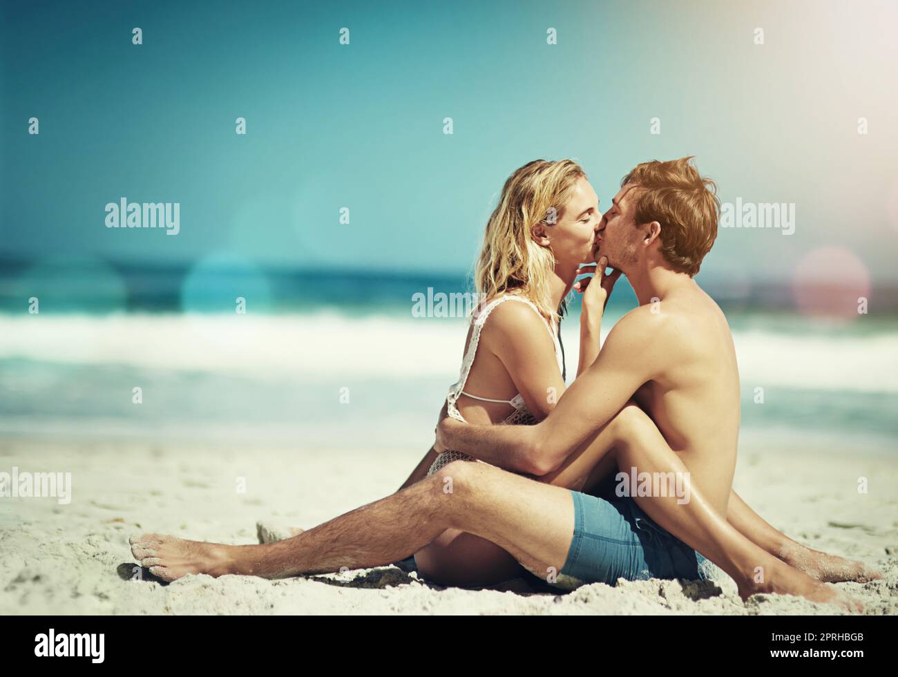 Halt die Klappe und küsse mich. Ganzkörperaufnahme eines liebevollen jungen Paares, das von Angesicht zu Angesicht am Strand sitzt. Stockfoto