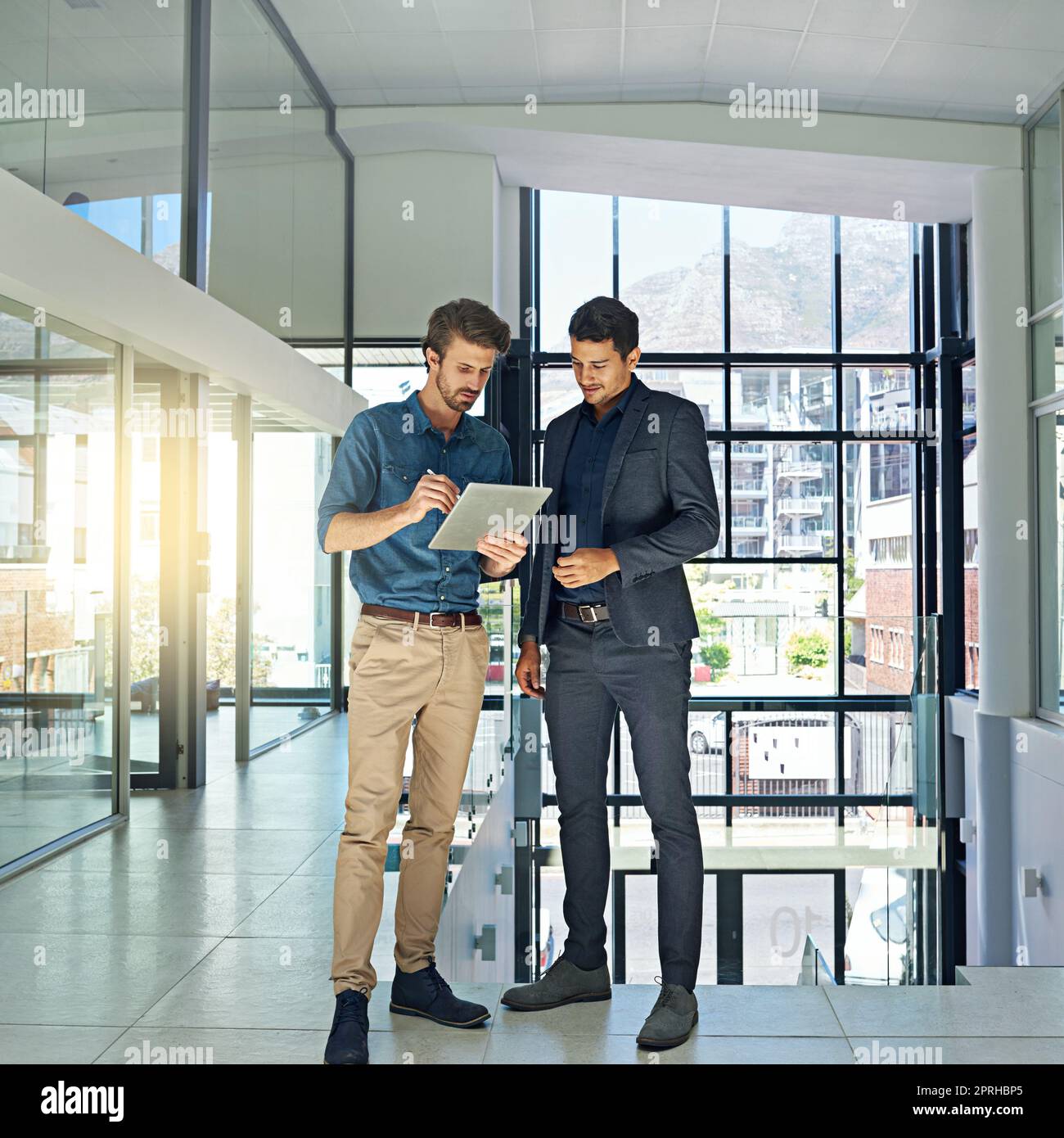 Daten und Fakten synchronisieren: Zwei Kollegen sprechen über ein digitales Tablet, während sie in einem modernen Büro stehen. Stockfoto
