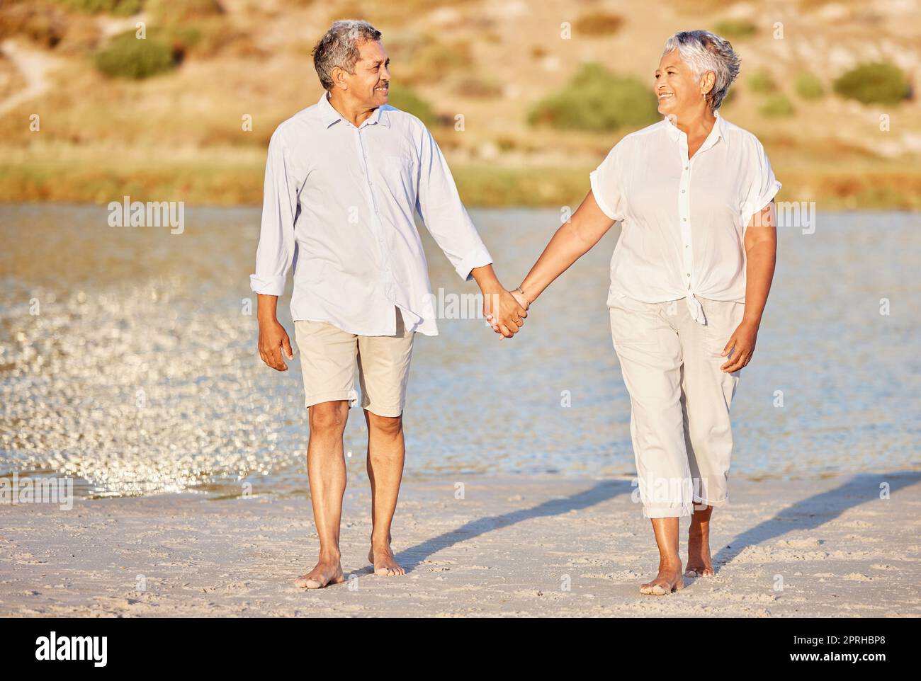 Liebe, Wandern und Seniorenpaar auf einem Strandsee zusammen für Ruhe, Entspannung und romantisches Meer, Wasser oder Meeresdate. Ältere glückliche Menschen, Mann und Frau lächeln, während sie Renten- und Rentenleben leben Stockfoto