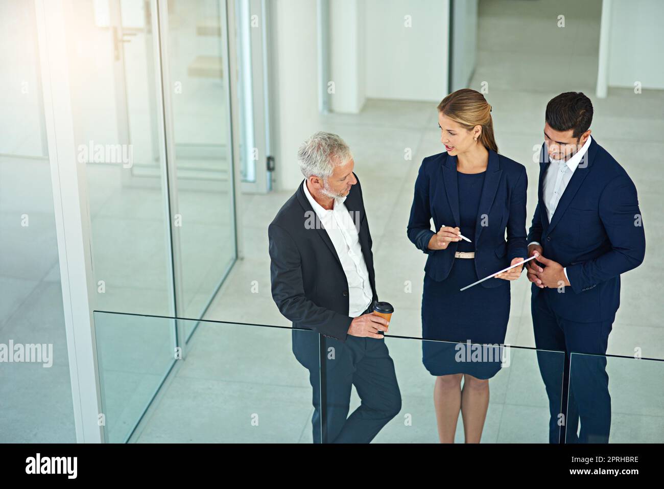 Ihre Entscheidungen bringen das Unternehmen voran. Drei Kollegen sprechen über ein digitales Tablet, während sie in einem modernen Büro stehen. Stockfoto