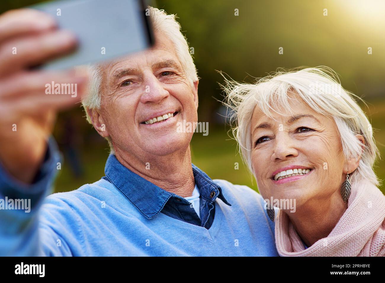 Breites Lächeln für die Aufnahme. Ein Seniorenpaar, das zusammen in einem Park ein Foto gemacht hat. Stockfoto