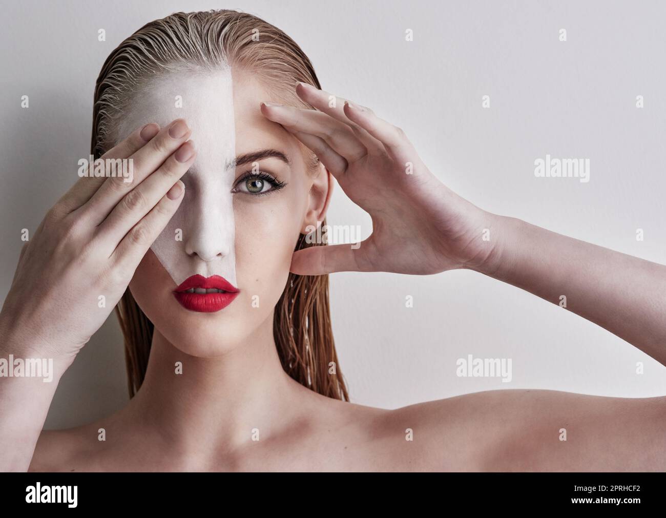 Zeigen Sie Ihre wahren Farben. Eine schöne Frau trägt Gesichtsfarbe und roten Lippenstift vor einem einfachen Hintergrund. Stockfoto