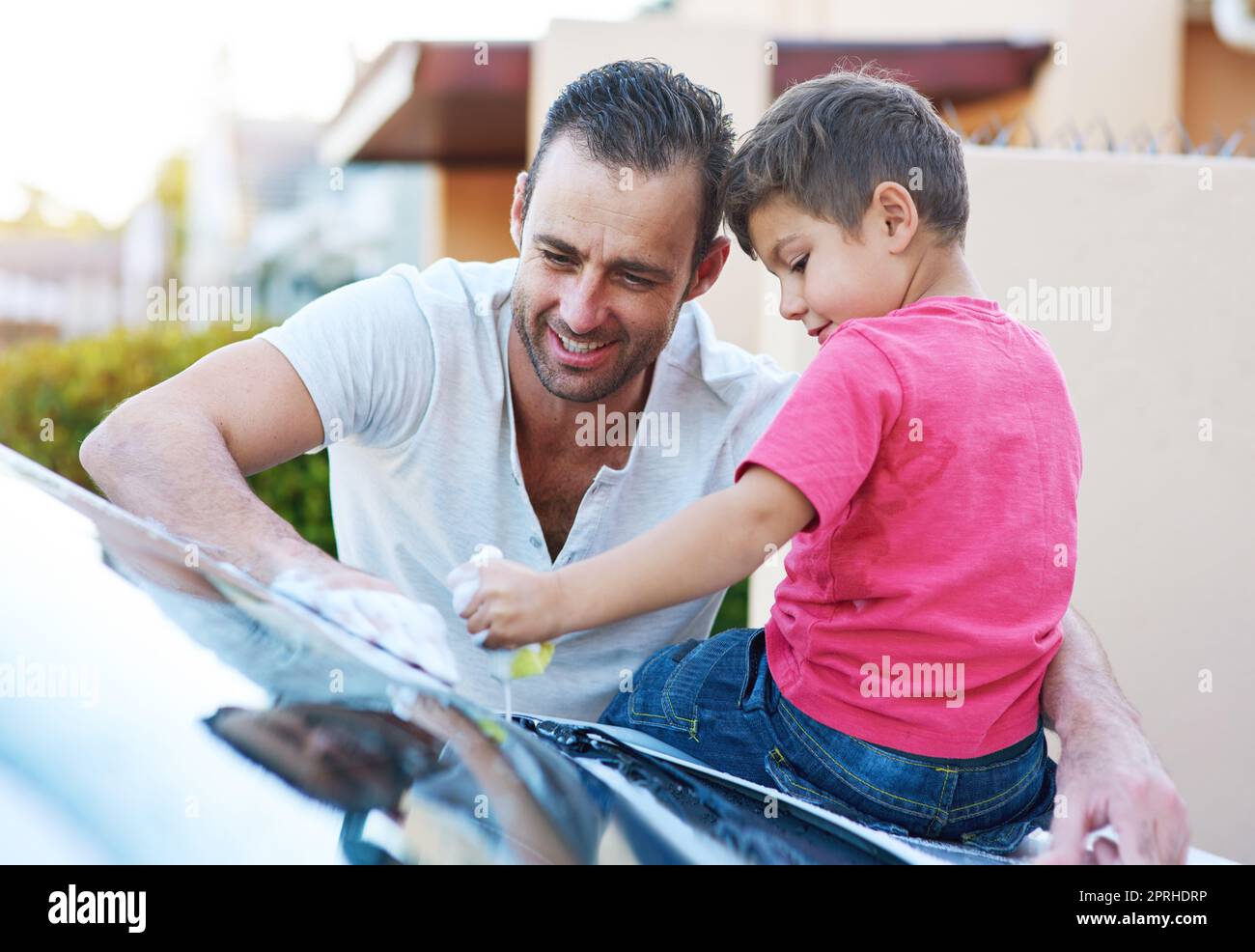 Daddys kleiner Helfer. Ein hübscher Vater und sein Sohn waschen zusammen ein Auto. Stockfoto