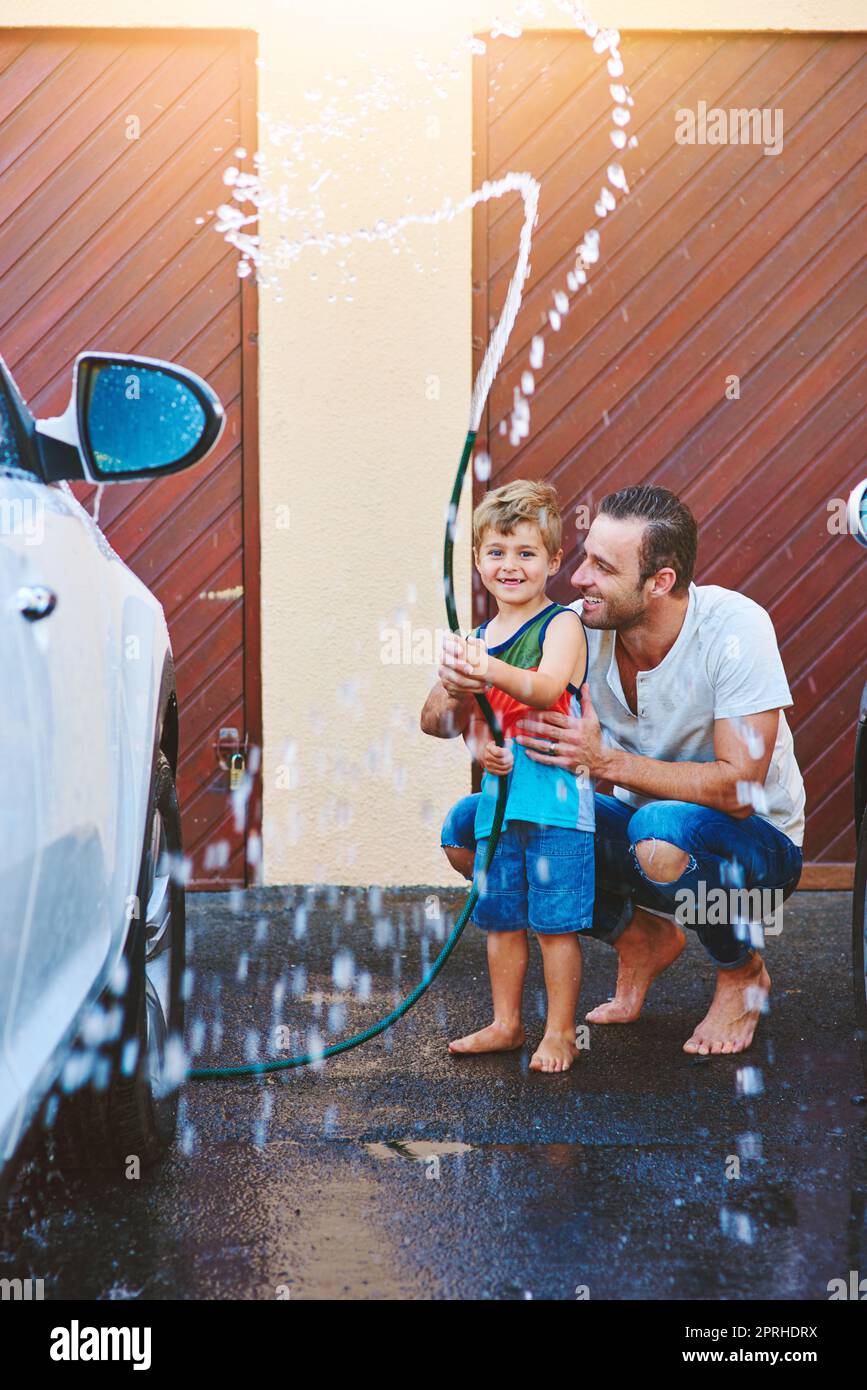 Es gibt Spaß zu haben, während der Arbeit zu tun. Die ganze Aufnahme eines Vaters und eines Sohnes, die mit einer Schlauchleitung spielen, während sie ein Auto gemeinsam waschen. Stockfoto