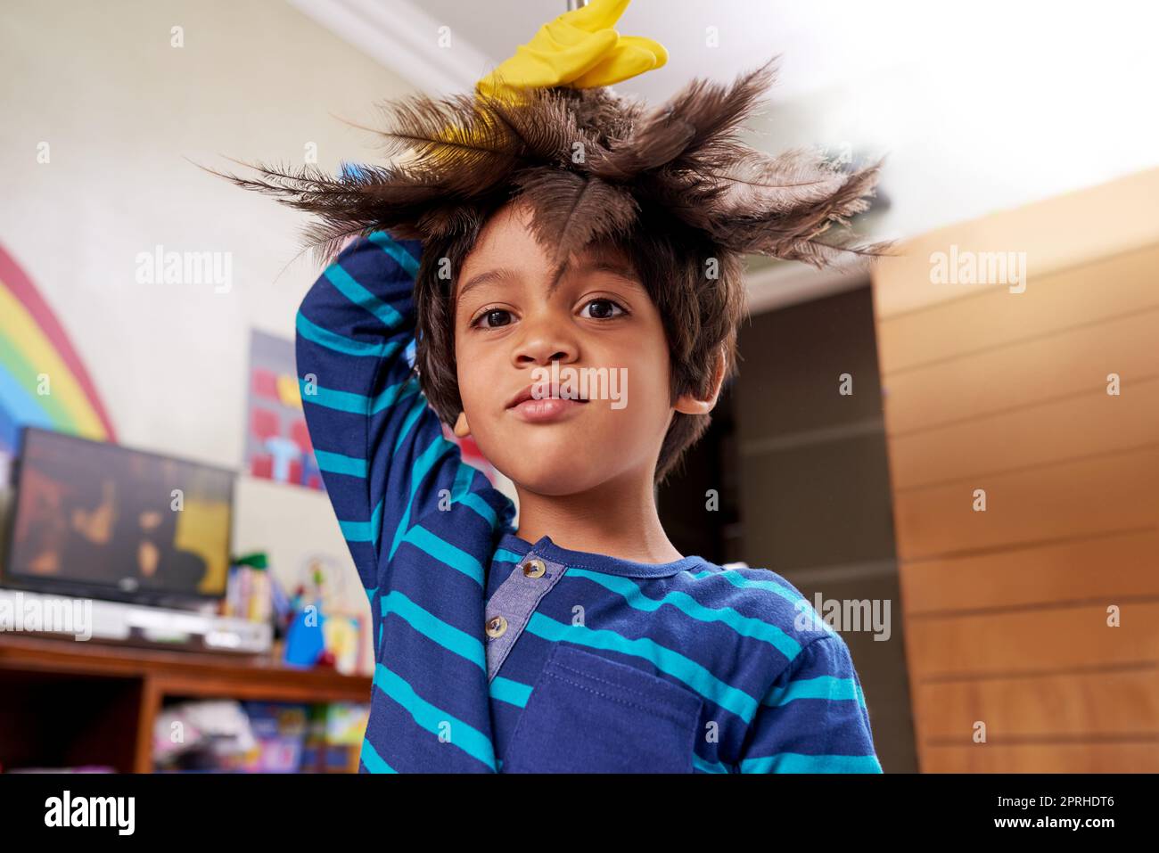 Aufgaben können auch Spaß machen. Porträt eines Jungen, der einen Federstaub auf seinem Kopf hält. Stockfoto
