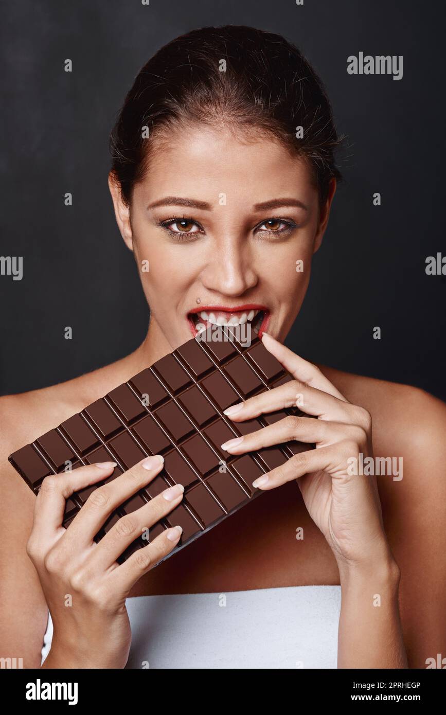 Man kann nie zu viel Schokolade haben. Studioaufnahme einer attraktiven jungen Frau, die in eine Schokoladenplatte beißt. Stockfoto