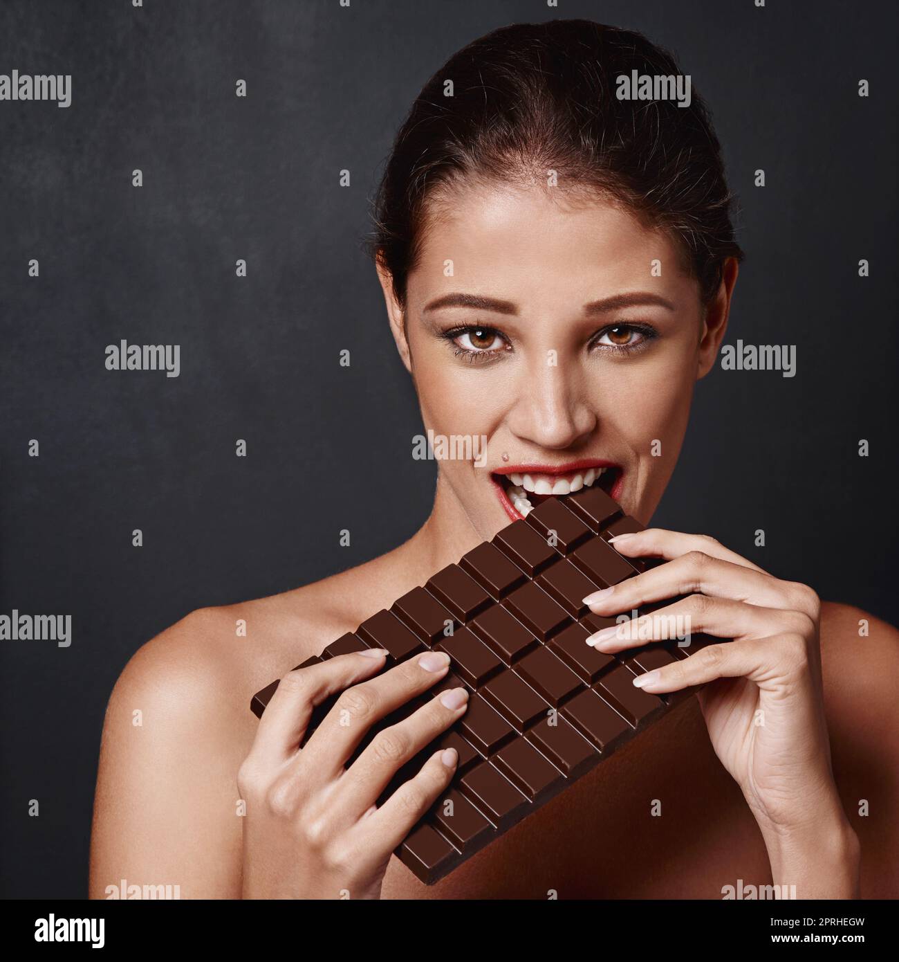 Ich kann nicht nein zu Schokolade sagen. Studioaufnahme einer attraktiven jungen Frau, die in eine Schokoladenplatte beißt. Stockfoto