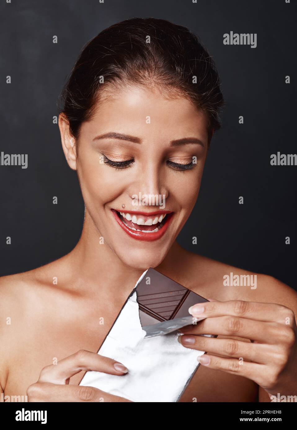 Schokolade ist die Antwort. Studioaufnahme einer attraktiven jungen Frau, die ein Stück Schokolade genießt. Stockfoto