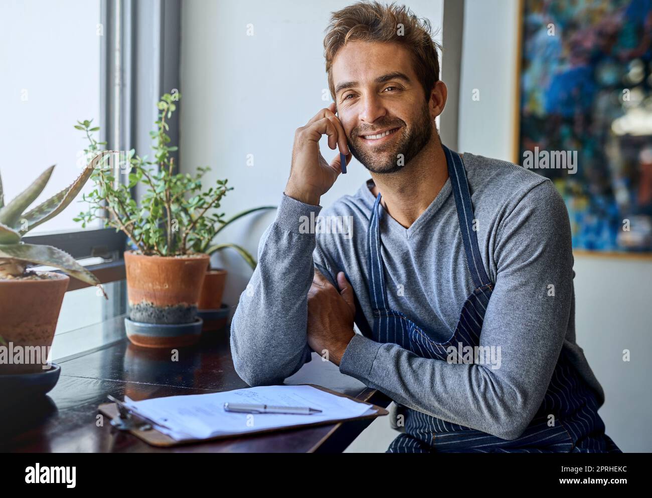 Barista und Geschäftseigentümer zusammen. Ein hübscher junger Barista, der ein Mobiltelefon benutzt, während er in seinem Coffee Shop arbeitet. Stockfoto
