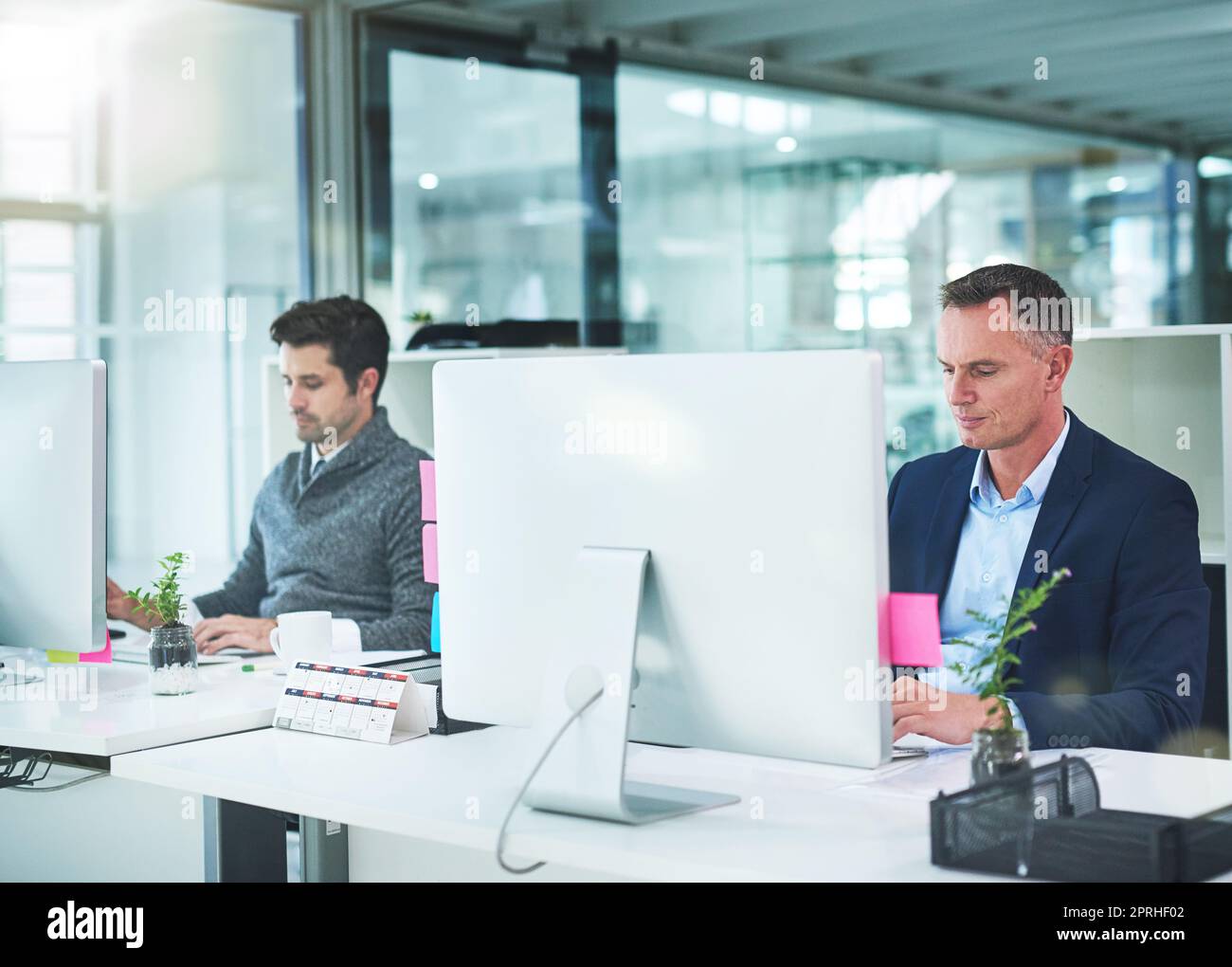 Arbeiten individuell für gemeinsamen Erfolg. Zwei Geschäftsleute arbeiten an ihren Schreibtischen im Büro. Stockfoto