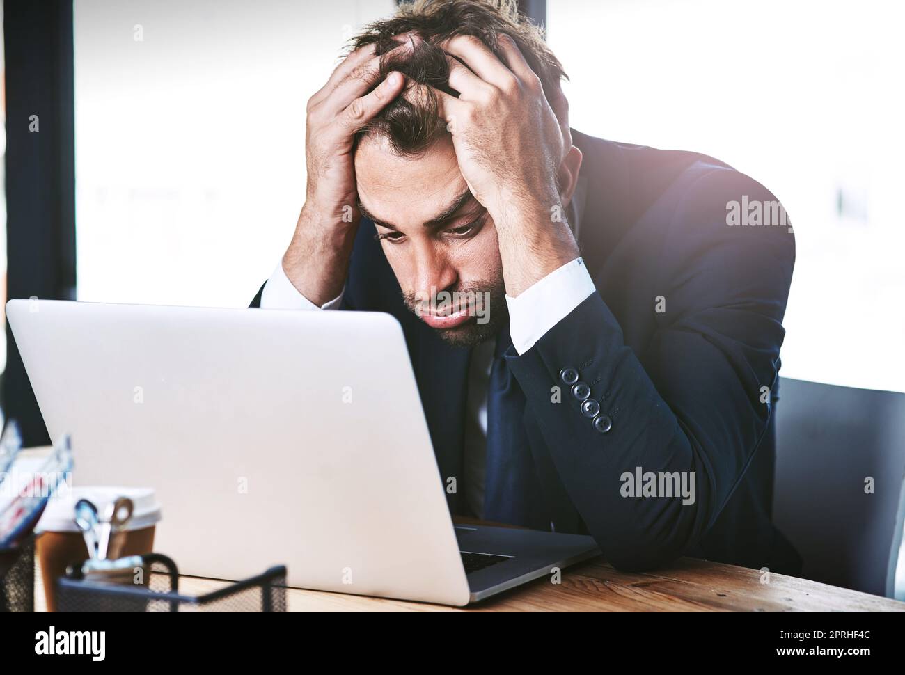 Er kann es einfach nicht herausfinden. Ein hübscher junger Geschäftsmann, der gestresst aussieht, während er im Büro an seinem Laptop arbeitet. Stockfoto