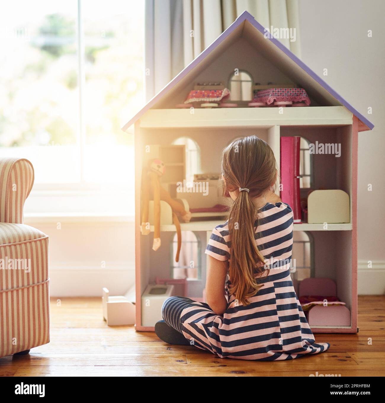 Ihren Puppen einen Platz zum Zuhause geben. Ein kleines Mädchen, das zu Hause mit einem Puppenhaus spielt. Stockfoto