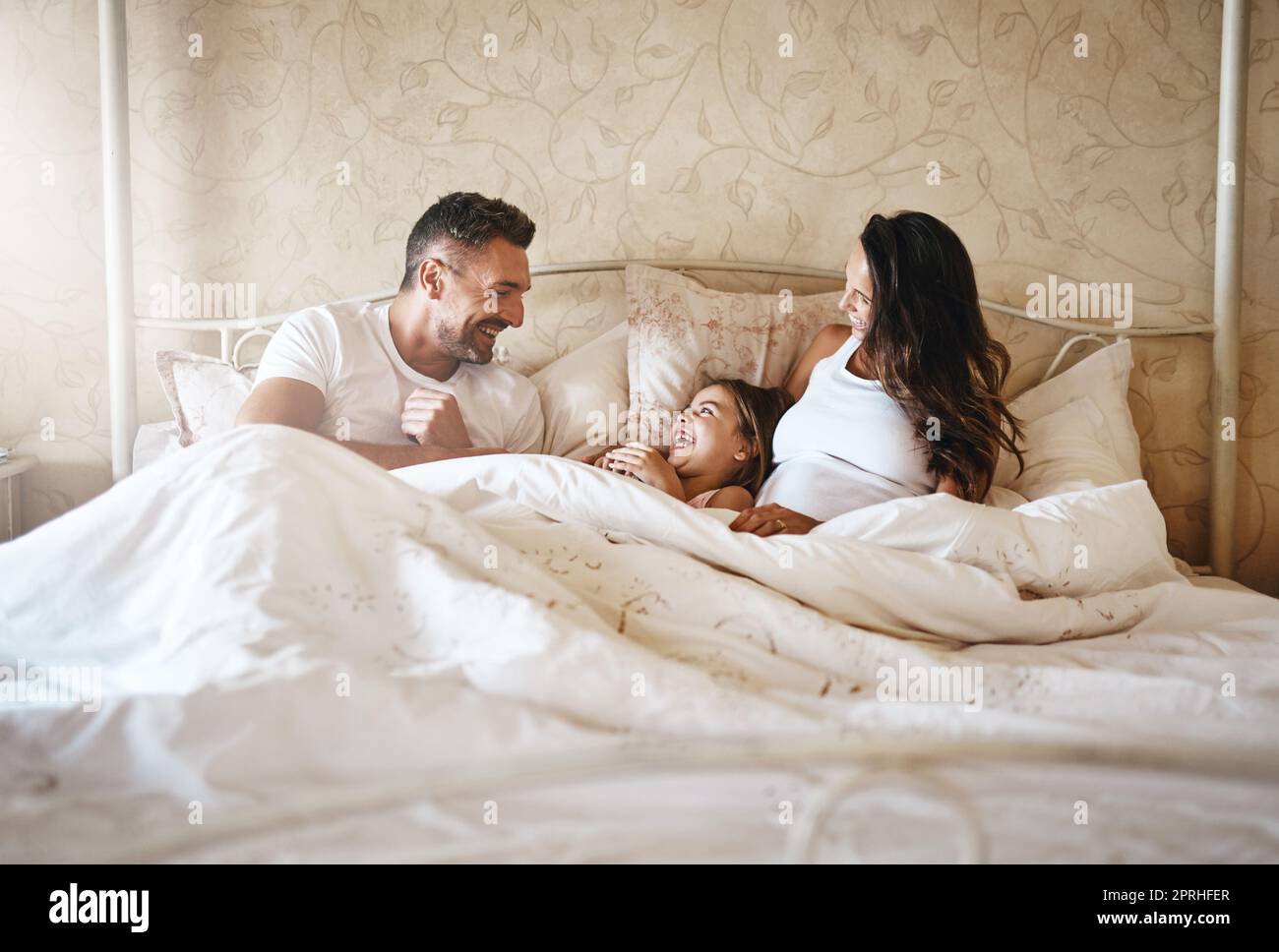 Nichts kommt einer liebevollen Familie nahe. Ein glückliches kleines Mädchen, das mit ihrem Vater und ihrer Schwangeren im Bett liegt. Stockfoto