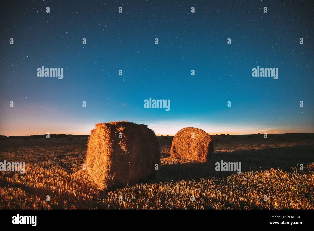 Comet Neowise C2020 F3 in Night Starry Sky über Heuhaufen im Summer Agricultural Field. Nachtstars Über Der Ländlichen Landschaft Mit Heuballen Nach Der Ernte. Landwirtschaftskonzept Stockfoto