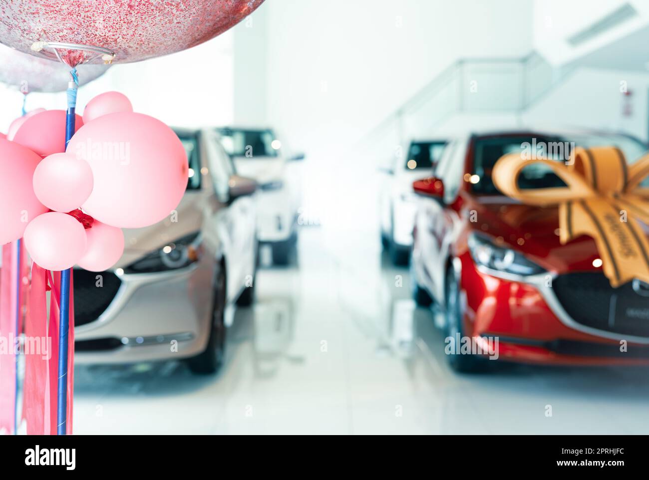 Pinke Ballons auf einem verschwommenen Auto, das in einem luxuriösen Ausstellungsraum geparkt ist. Neues Auto in modernem Ausstellungsraum geparkt. Büro des Autohändlers. Kfz-Leasing- und Versicherungskonzept. Autovermietungsgeschäft. Händler für Elektrofahrzeuge. Stockfoto