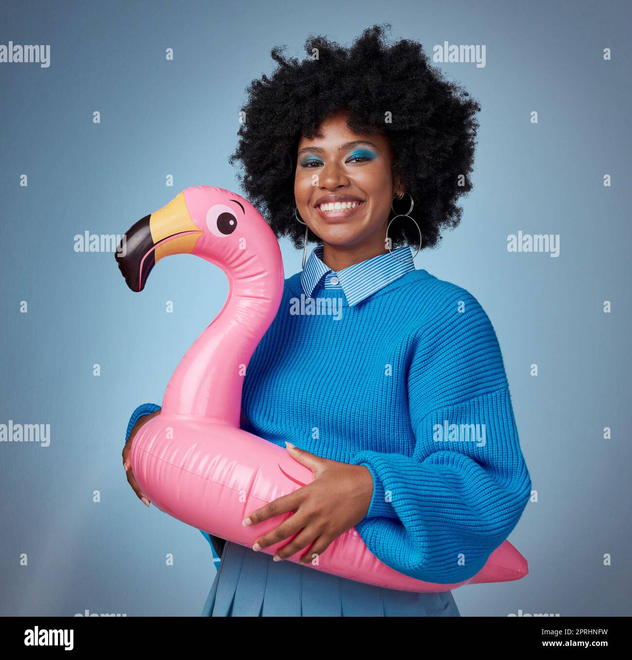 Porträt einer Frau in Blau mit einem Flamingo und einem Lächeln im Gesicht. Glückliche schwarze Frau mit aufblasbarem Vogelgummiring auf Hüfte auf blauem Hintergrund. Mocku Stockfoto