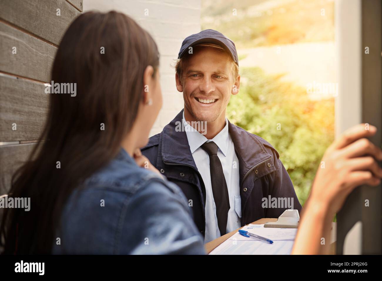 Empfang eines Pakets von ihrem freundlichen Lieferer. Ein junger Mann, der eine Lieferung an eine Frau zu Hause macht Stockfoto