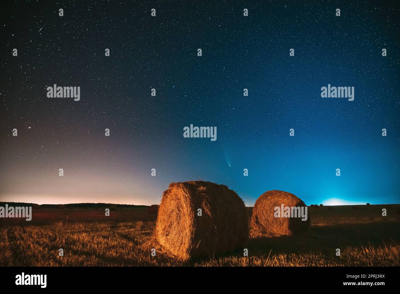Comet Neowise C2020 F3 in Night Starry Sky über Heuhaufen im Summer Agricultural Field. Nachtstars Über Der Ländlichen Landschaft Mit Heuballen Nach Der Ernte Stockfoto