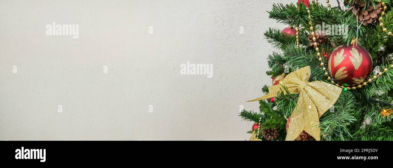 Ein Banner mit einem Weihnachtsbaum, dekoriert mit goldenen Schleifen, glitzernden Glaskugeln und Weihnachtsbaumspielzeug auf hellem Hintergrund und einem leeren Kopierbereich auf der linken Seite Stockfoto