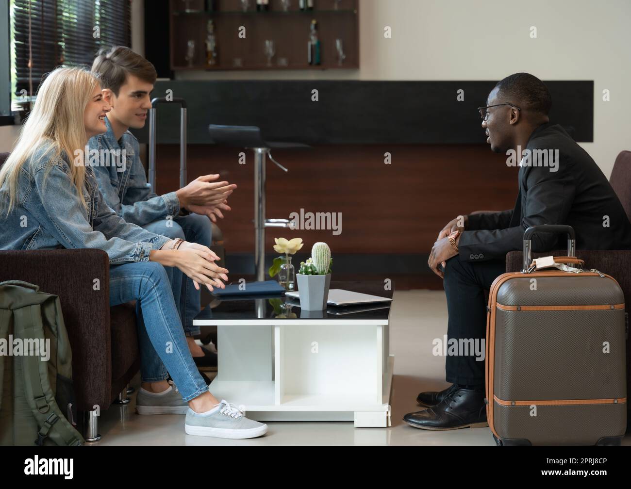 Lächelnde, vielfältige Reisende, die in der Flughafenlounge sitzen und sich unterhalten. Stockfoto