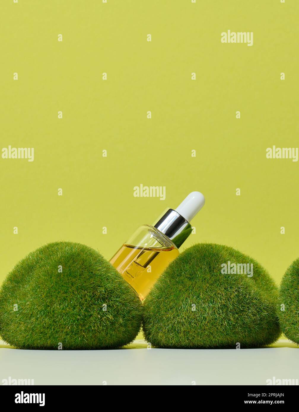 Transparente Glasflasche mit Pipette und gelbem Öl auf grünem Moos Stockfoto