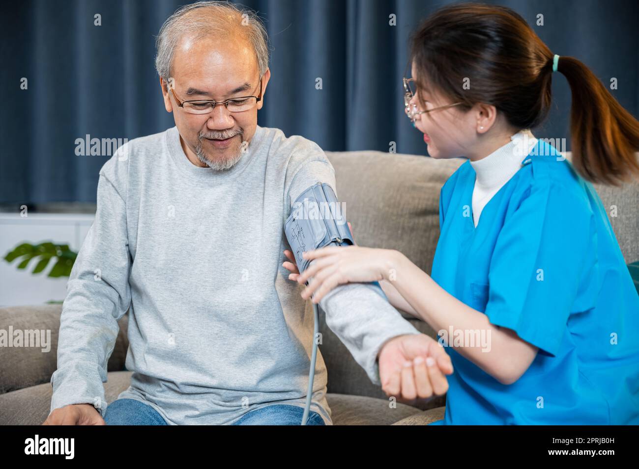 Asiatische Krankenschwester besucht Patienten Seniorenarzt zu Hause sie misst den arteriellen Blutdruck am Arm Stockfoto