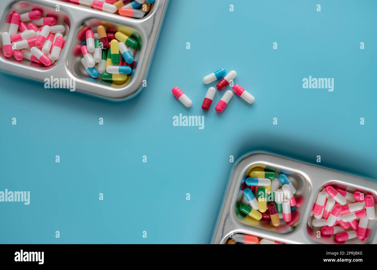 Hochwinkel-Ansicht mehrfarbiger Antibiotikakapseln auf Edelstahltablett und blauem Hintergrund. Antibiotikaresistenz. Verschreibungspflichtige Medikamente. Pharmazeutische Industrie. Herstellung von Kapselpillen. Stockfoto