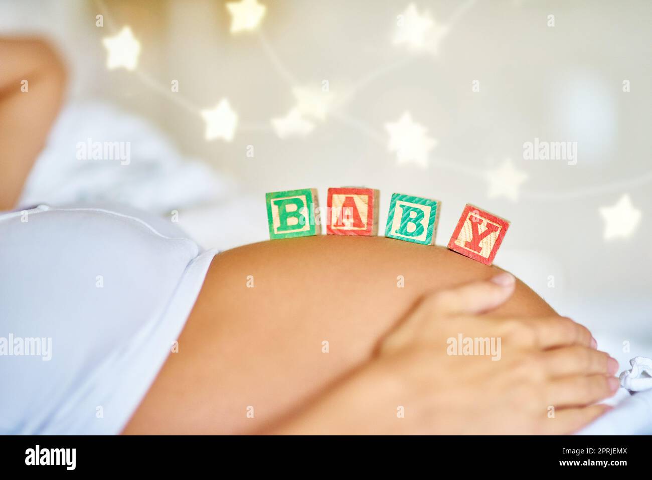 Baby an Bord. Nahaufnahme einer Schwangeren, die mit hölzernen Babyblöcken auf ihrem Bauch liegt. Stockfoto