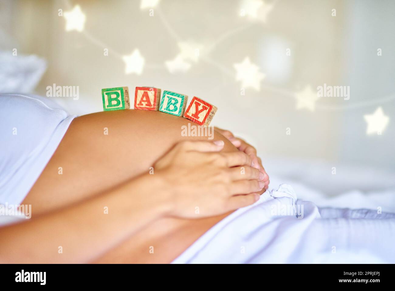 Demnächst verfügbar. Nahaufnahme einer Schwangeren, die mit hölzernen Babyblöcken auf ihrem Bauch liegt. Stockfoto