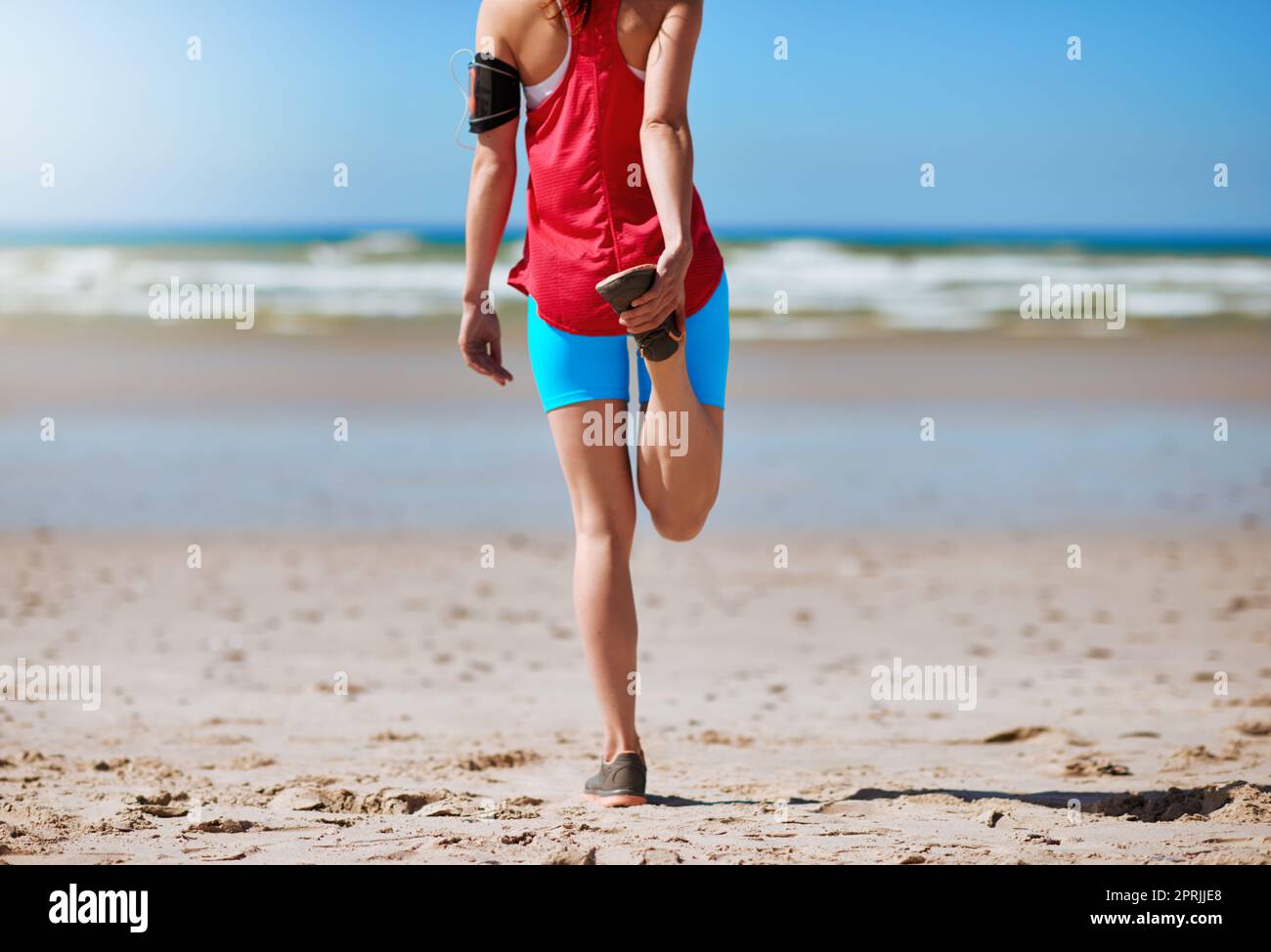 Du musst dich strecken, wenn du Verletzungen vermeiden willst. Rückansicht einer jungen Frau, die sich vor ihrem Lauf am Strand ausdehnt. Stockfoto