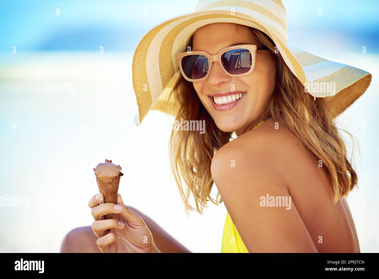 Abkühlung an einem heißen Tag. Porträt einer schönen jungen Frau, die am Strand ein Eis isst. Stockfoto