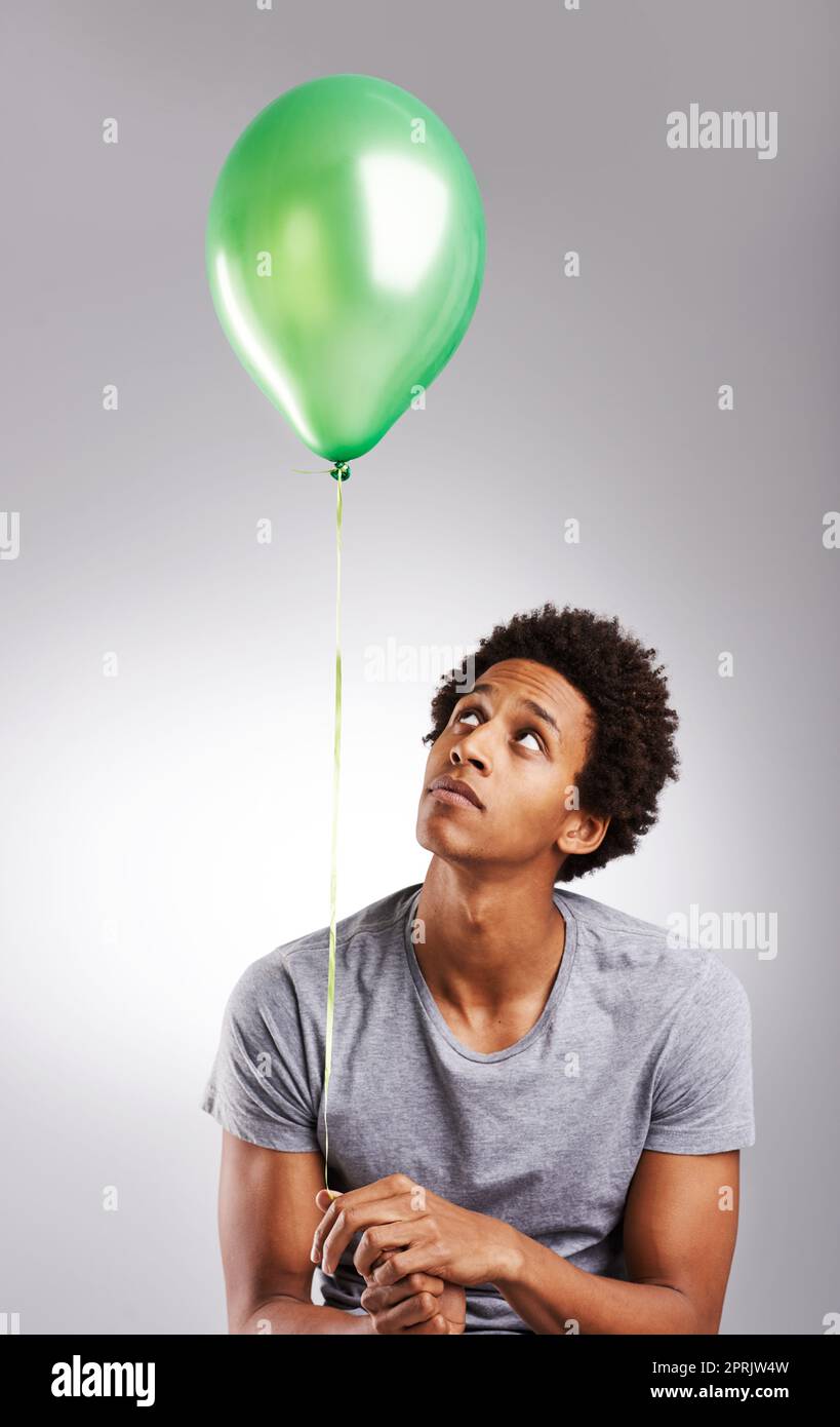Ein junger Mann hält einen Ballon über einem grauen Hintergrund. Stockfoto