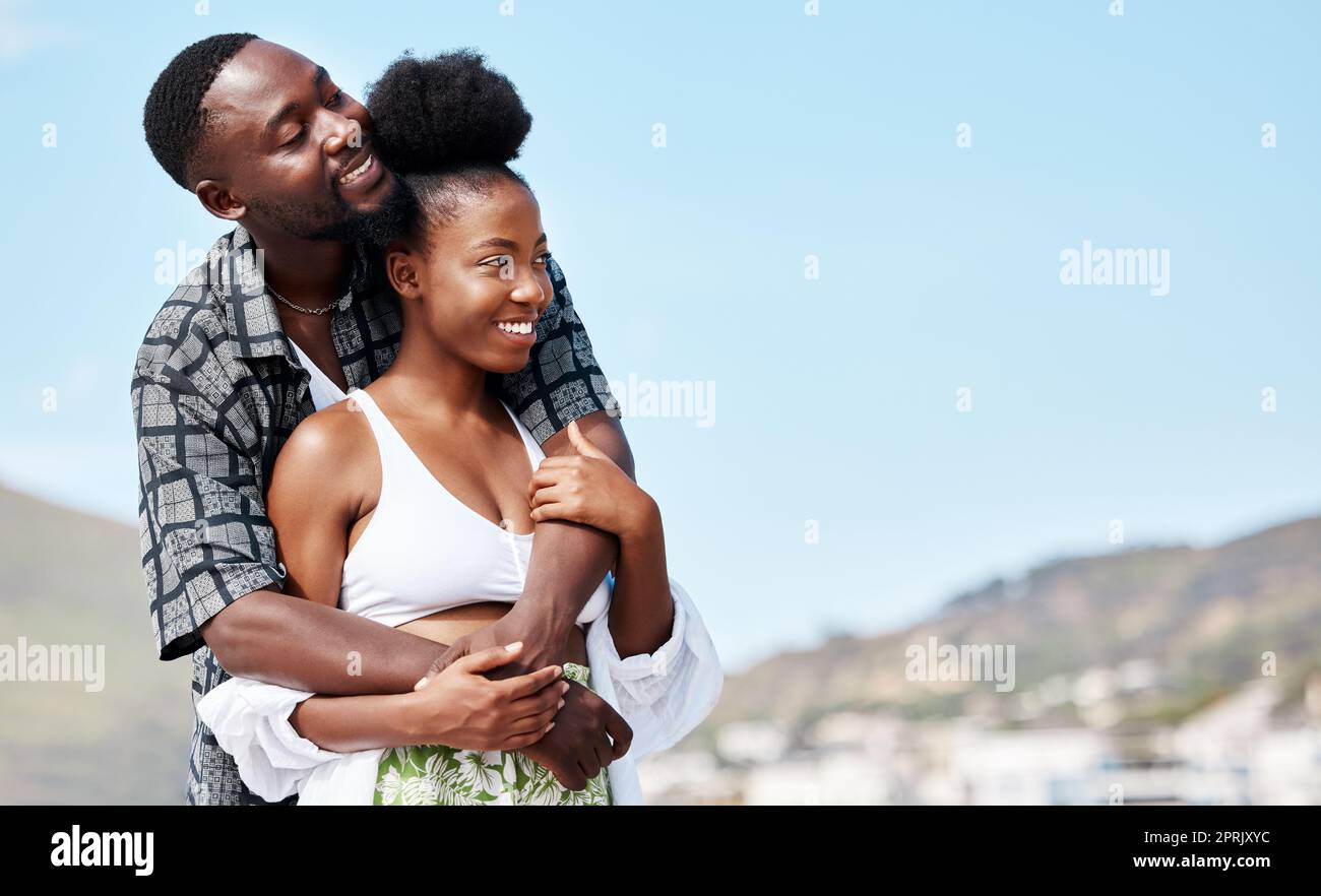 Ein junges, liebes und schwarzes Paar umarmt sich am Strand und verbindet sich in der blauen Landschaft am Meer. Glückliche afroamerikanische Menschen in fröhlichen Beziehungen umarmen sich bei einem friedlichen Date im Freien. Stockfoto
