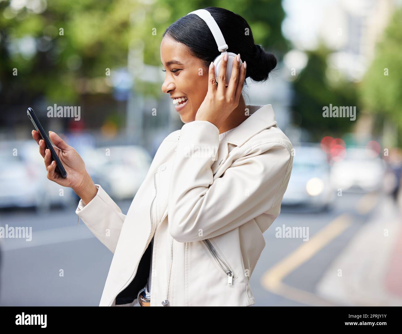Glückliches Stadtmädchen mit Telefon und Kopfhörern bei Videogesprächen während des Spaziergangs Entspannen Sie sich auf der Straße zur Arbeit oder zu Hause. Schwarze Frau oder Schülerin, die über einen Witz, ein Meme oder ein Online-Video lacht, während sie an einen Ort reisen Stockfoto