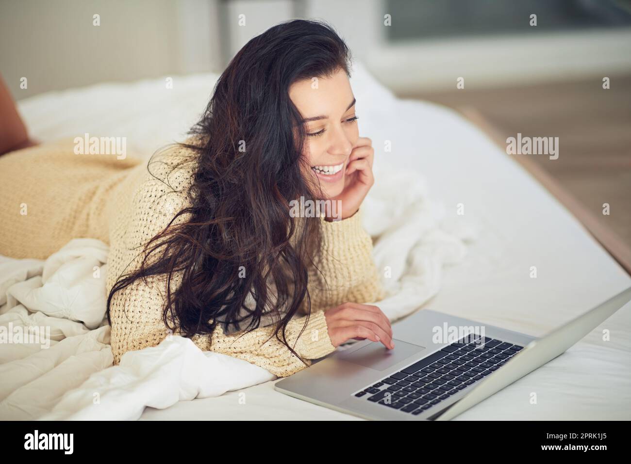 Eine junge Frau, die ihren Laptop benutzt, während sie auf ihrem Bett liegt. Stockfoto