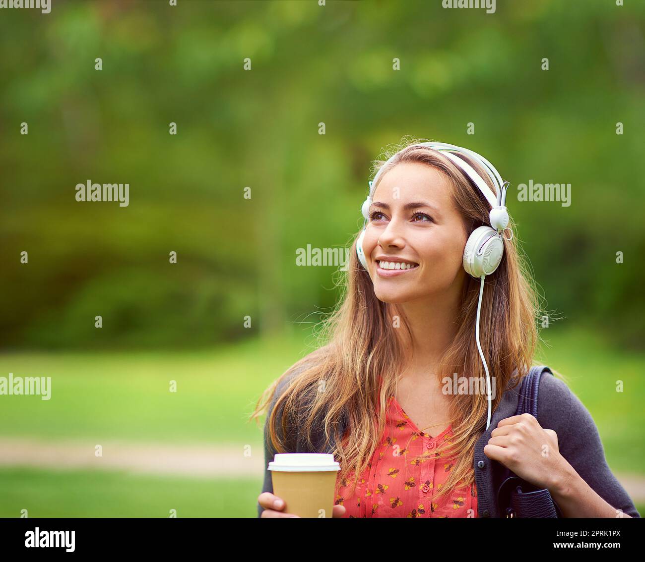 Machen Sie das Beste aus einem schönen Tag. Eine junge Frau, die Musik hört, während Sie unterwegs einen Kaffee trinken. Stockfoto