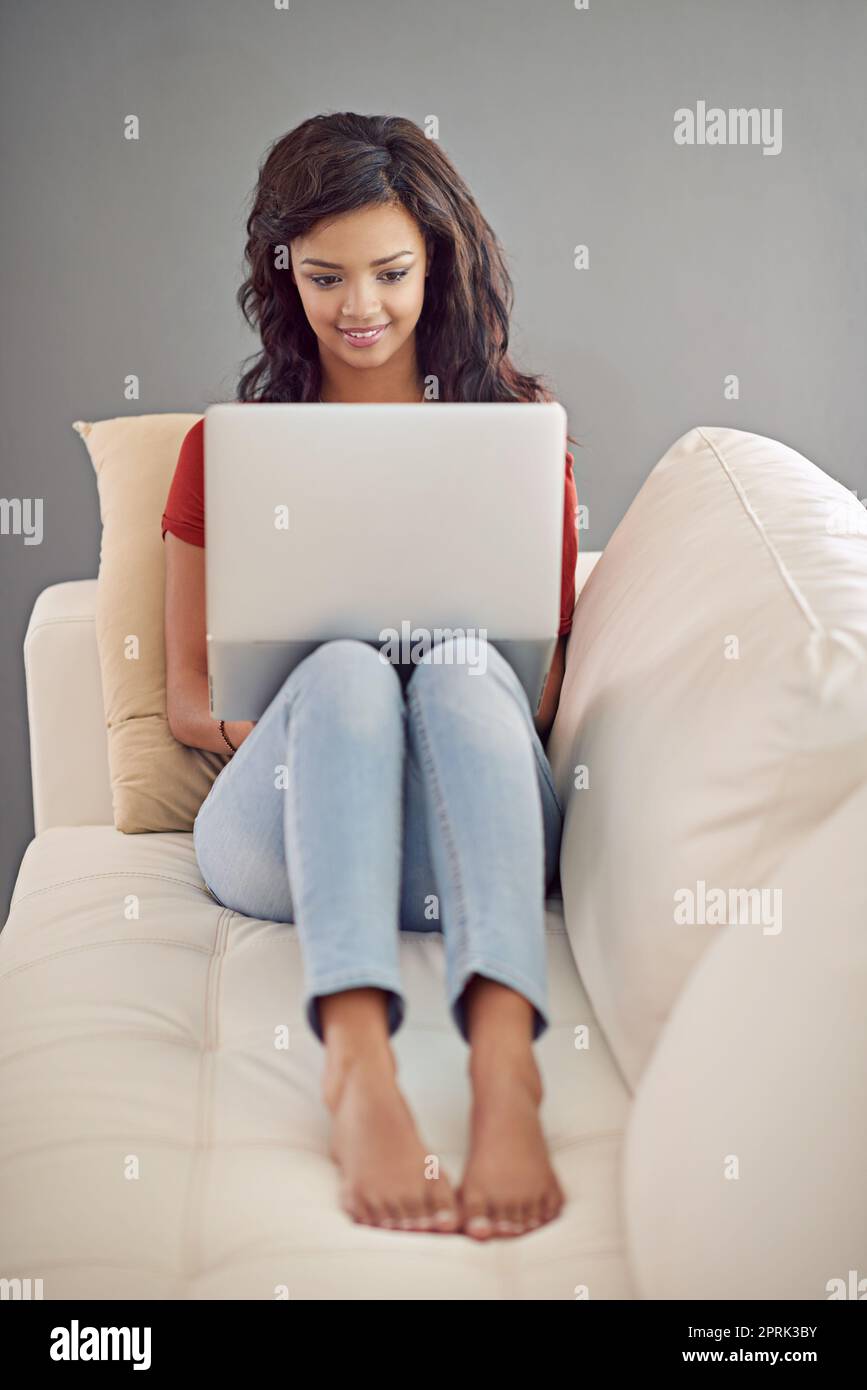 Antworten auf einige E-Mails. Ganzkörperaufnahme einer jungen Frau, die ihren Laptop benutzt, während sie sich zu Hause entspannt. Stockfoto