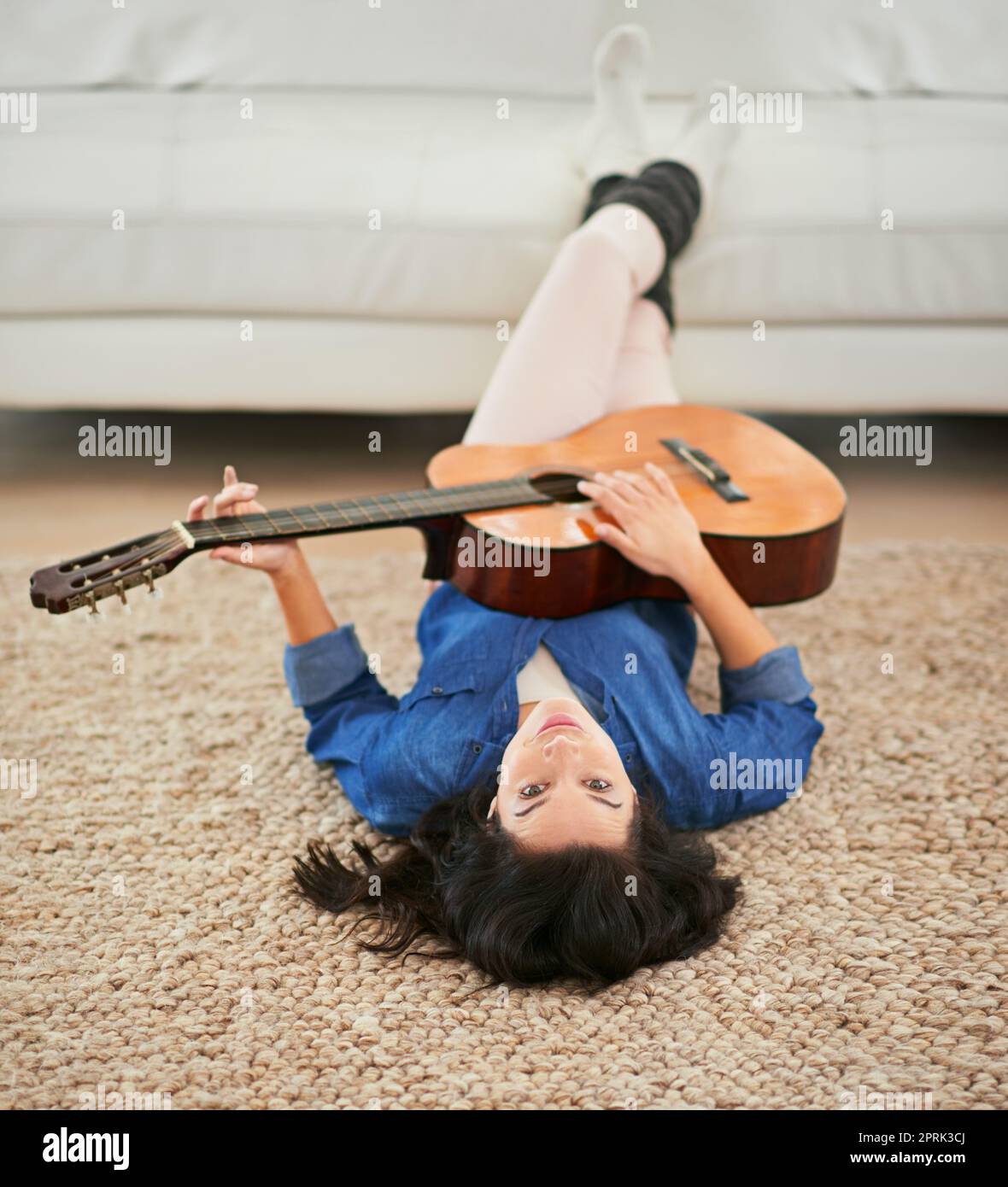 Musik ist das Essen von life...play On. Eine junge Frau spielt Gitarre, während sie auf ihrem Wohnzimmerboden liegt. Stockfoto