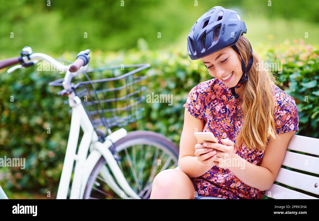 Eine junge Frau, die ein Telefon benutzt, während sie auf einem Fahrradweg im Park unterwegs ist. Stockfoto