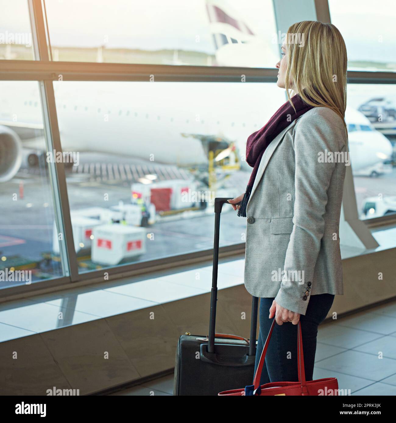 Eine junge Frau, die auf einem Flughafen steht und aus dem Fenster schaut. Stockfoto
