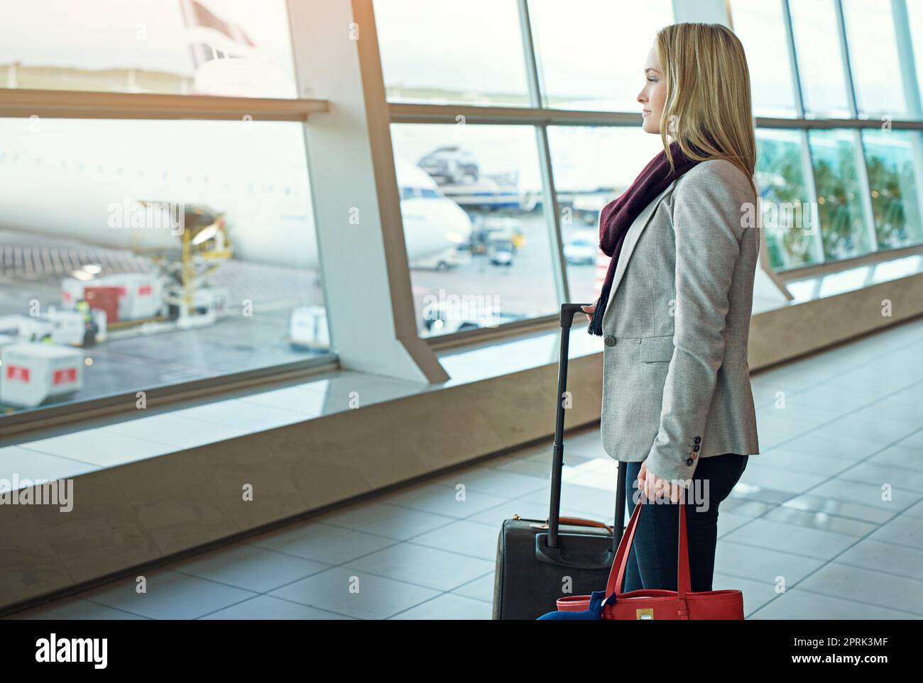Fast Zeit zum Start. Eine junge Frau, die auf einem Flughafen steht und aus dem Fenster schaut. Stockfoto