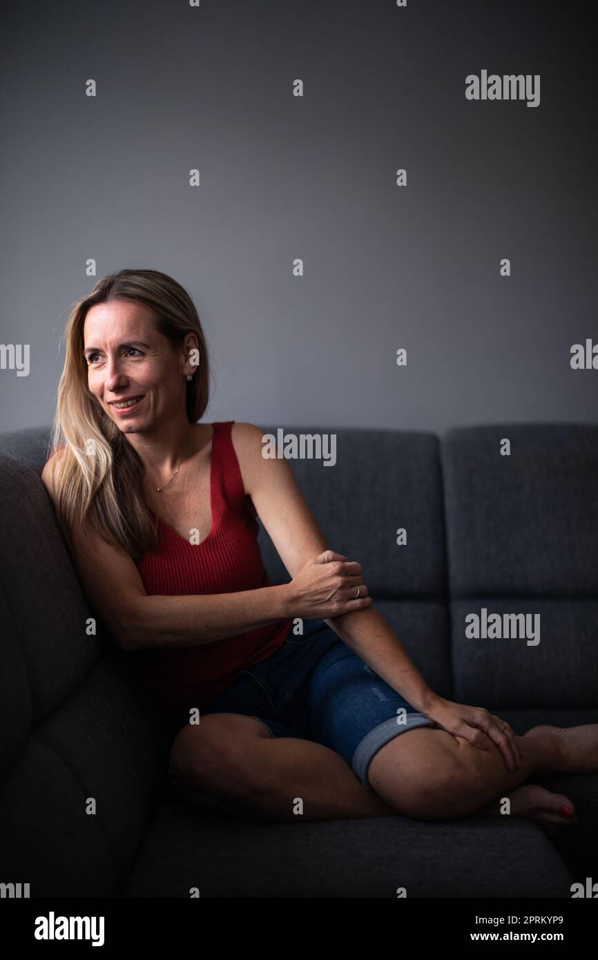 Frau mittleren Alters zu Hause, die sich auf einem Sofa entspannt (farblich abgetöntes Bild) Stockfoto