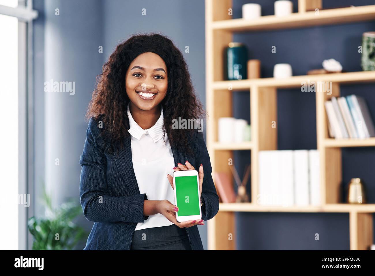 Jeder Unternehmer sollte das benutzen. Eine junge Geschäftsfrau mit einem Smartphone mit grünem Bildschirm in einem modernen Büro Stockfoto