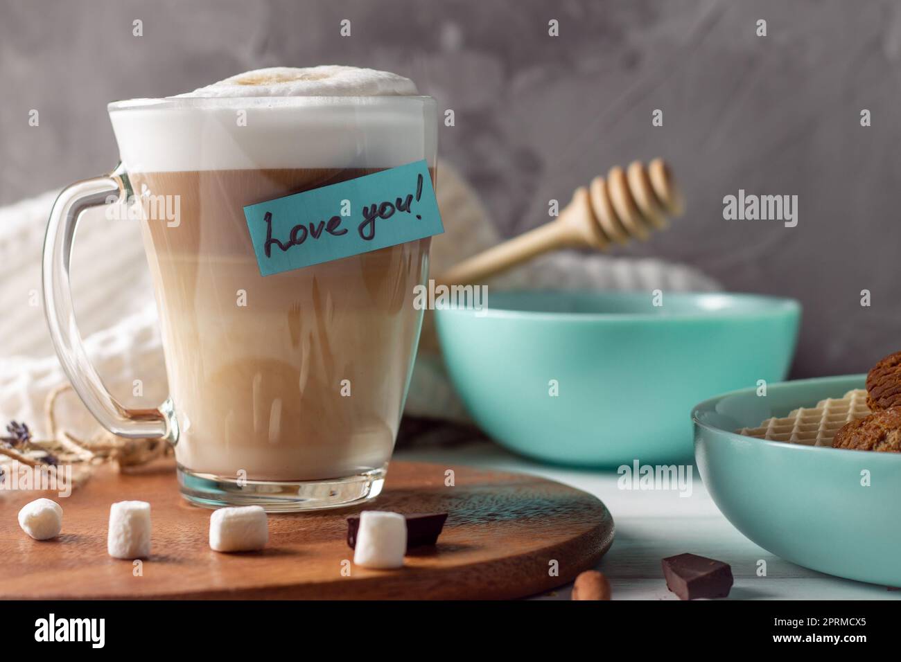 Kaffee Latte Tasse mit Love You Aufkleber auf Holztablett Mit türkisfarbenen Schalen mit Plätzchen und Marshmallows an der grauen Wand Hintergrund Stockfoto