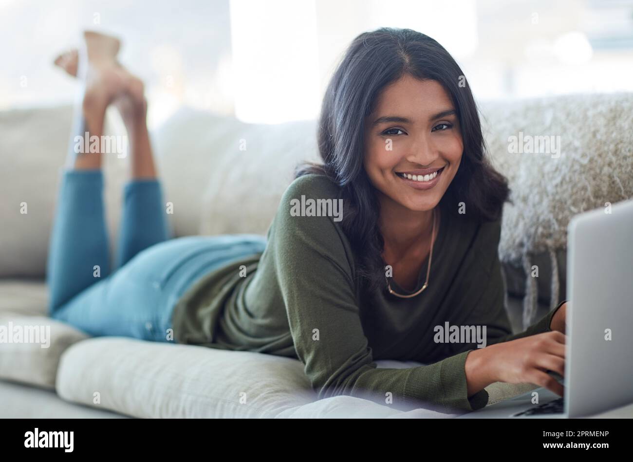 Immer auf dem Laufenden mit meinen Social-Media-Feeds. Porträt einer attraktiven jungen Frau, die ihren Laptop benutzt, während sie zu Hause auf dem Sofa liegt. Stockfoto