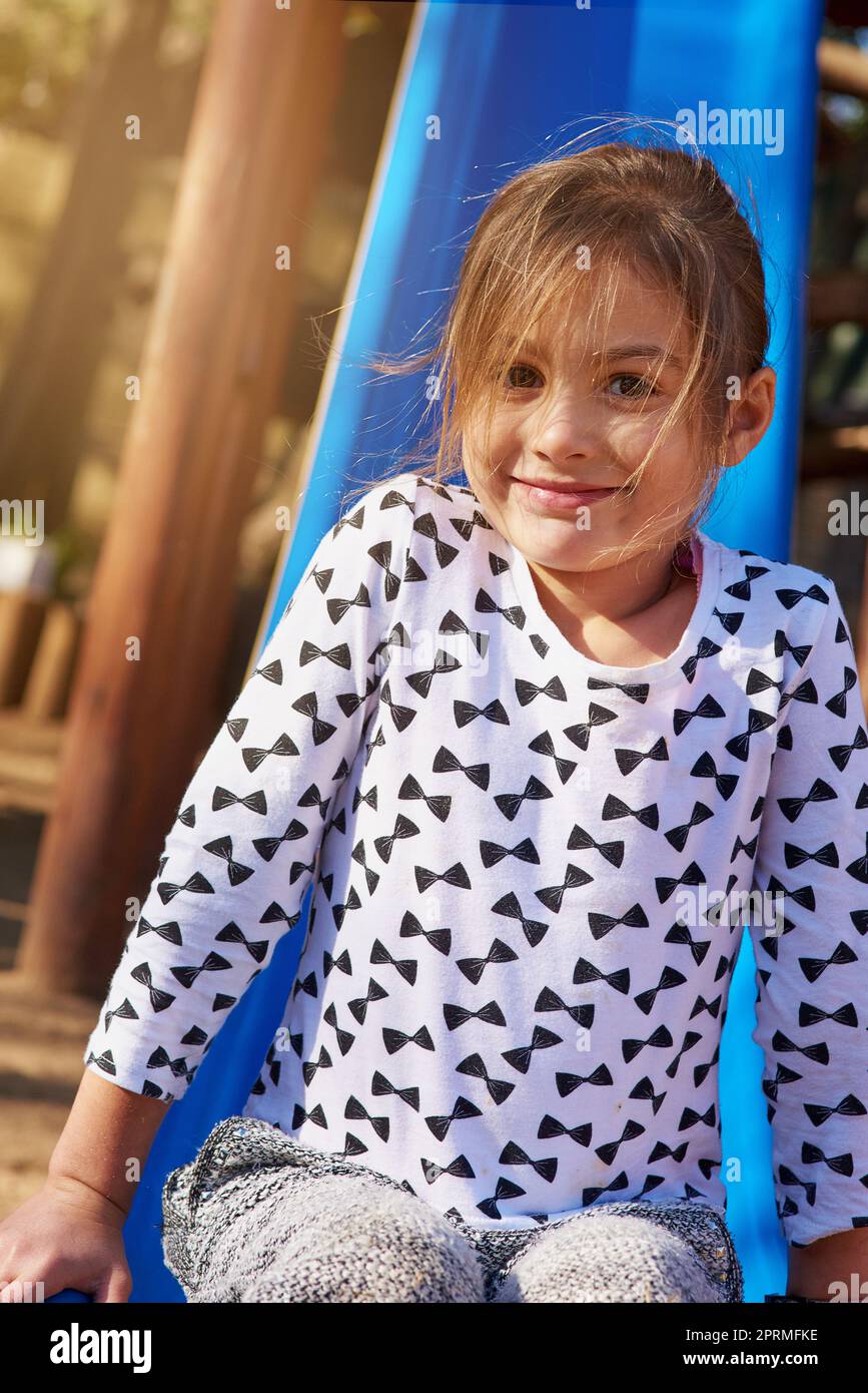 Nur ein weiterer Tag voller Spaß im Park. Porträt eines kleinen Mädchens, das auf einer Rutsche im Park spielt. Stockfoto