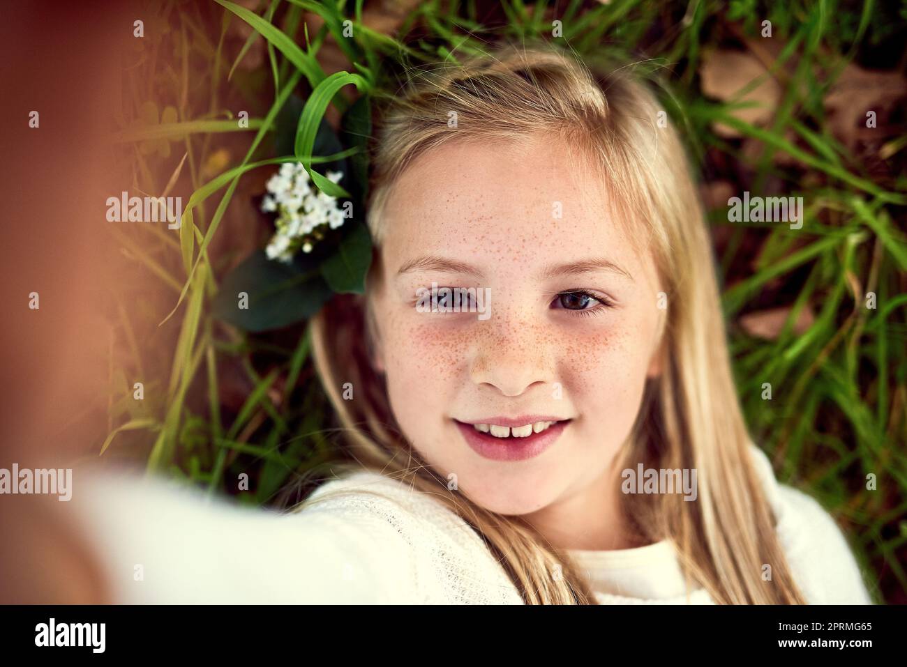 Glückseligkeit in der Kindheit. Porträt eines jungen Mädchens, das ein Selfie gemacht hat, während es draußen auf dem Gras liegt. Stockfoto